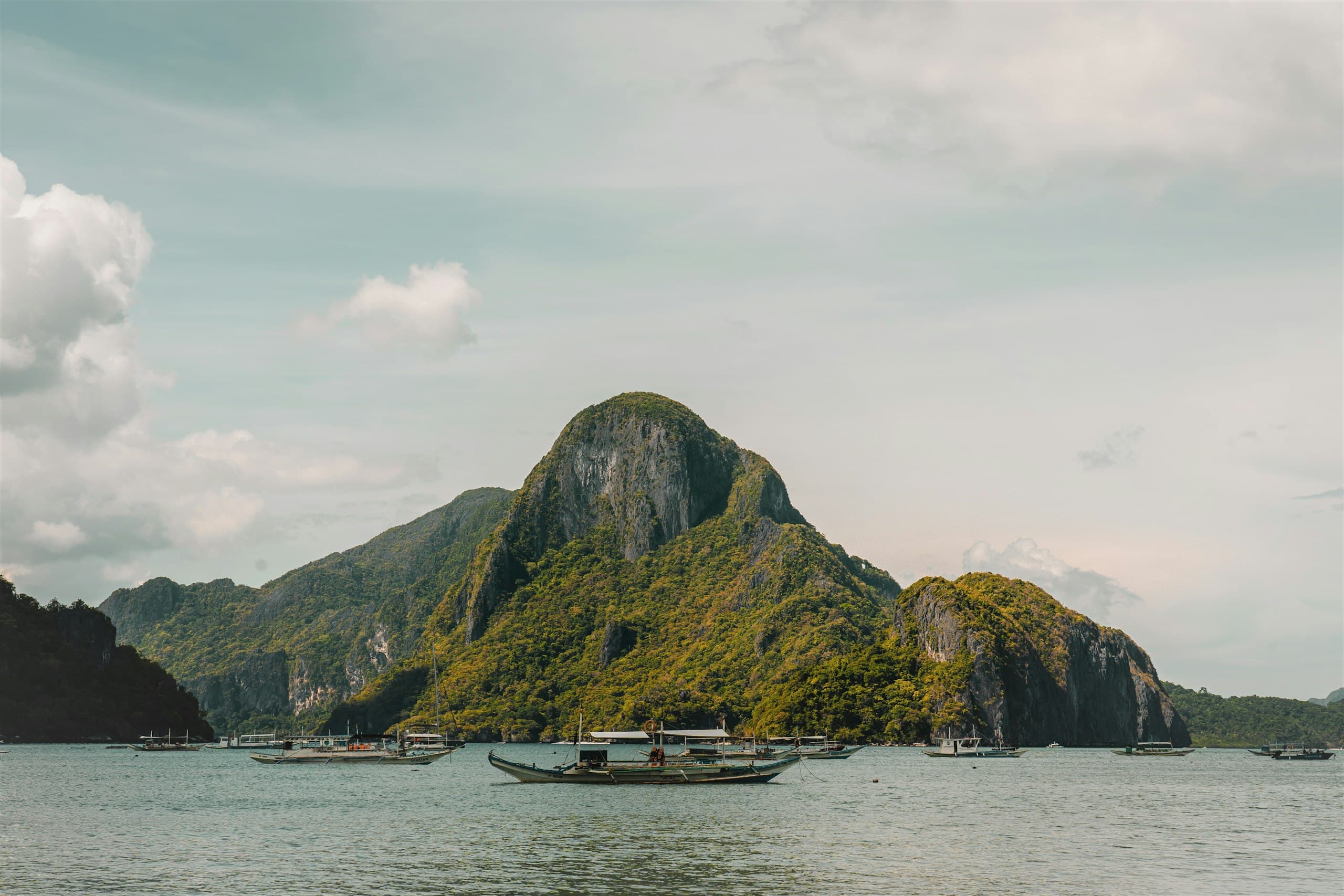 Outrigger boats resting on calm green water beneath the forested karst islands of El Nido, Palawan